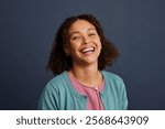 Joyful casual woman showing genuine smile while looking at camera over blue background. Close up face of a cheerful mixed race woman with a big smile. Radiant multiethnic girl laughing on blue wall.