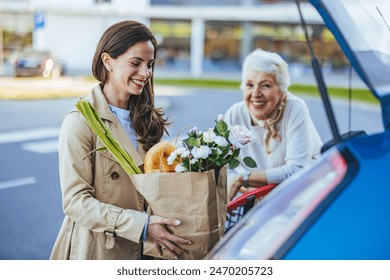 A joyful Caucasian adult daughter places fresh groceries into a car trunk, assisted by her smiling senior mother, symbolizing family care and support in a parking lot setting. - Powered by Shutterstock