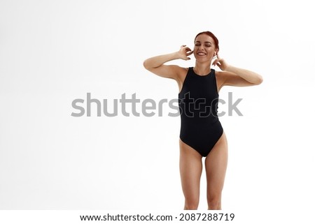Joyful caucasian female ballet dancer listening music in earphones. Concept of modern technologies. Pretty girl with red hair and wearing leotard. Isolated on white background in studio. Copy space