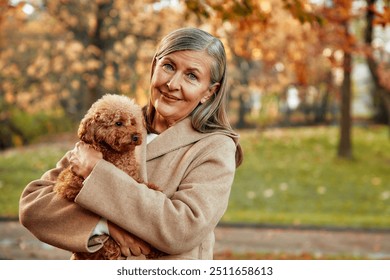 A joyful and cheerful woman holds her beloved poodle close to her side, surrounded by the vibrant beauty of autumn foliage in a tranquil sunlit park, capturing a moment of pure happiness and peace - Powered by Shutterstock