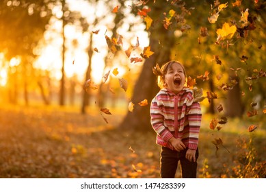 Joyful Child Enjoying The Fall Of Autumn Leaves On Her