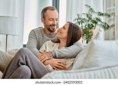 joyful child-free couple embracing and looking at each other on couch in living room, love and joy - Powered by Shutterstock