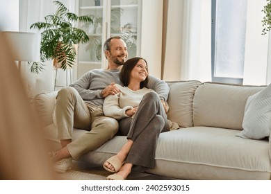 joyful child-free couple relaxing on cozy sofa in living room and looking away, leisure in comfort - Powered by Shutterstock