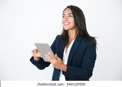 Joyful Confident Business Woman Using Tablet And Looking Away. Happy Young Latin Woman In Office Jacket Holding Mobile Pc And Staring Into Distance With Interest. Tablet Using Concept