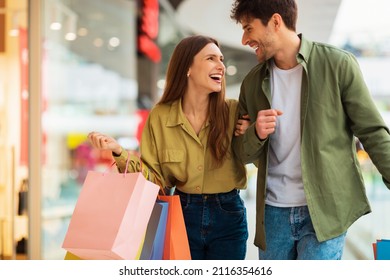Joyful Couple Carrying Shopping Bags And Laughing Smiling To Each Other Spending Time In Mall On Weekend. Happy Buyers Buying Clothes During Seasonal Sales. Commerce And Shopaholism Concept - Shutterstock ID 2116354616