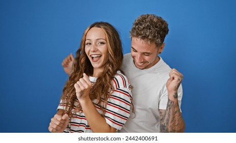 A joyful couple dances against a vibrant blue background, showcasing happiness and chemistry between the woman and man. - Powered by Shutterstock