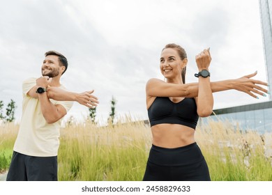 A joyful  couple in fitness attire stretching in an open field near a modern building, under a cloudy sky, displaying wearable technology.

 - Powered by Shutterstock