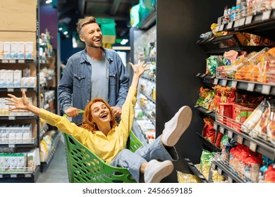 Joyful couple having fun while buying food in supermarket, happy man pushing shopping cart with his wife sitting inside - Powered by Shutterstock