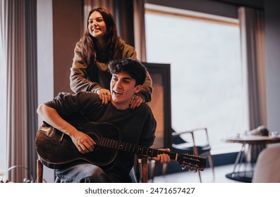 A joyful couple at home with the man playing guitar and the woman standing behind him, both smiling and having a good time. - Powered by Shutterstock