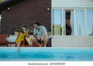 A joyful couple kneels by a poolside laughing and enjoying each other's company with a house backdrop - Powered by Shutterstock