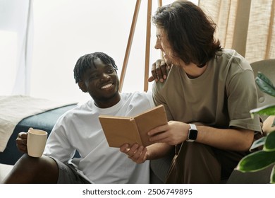 A joyful couple relaxes at home, sharing laughter while reading and sipping hot beverages. - Powered by Shutterstock