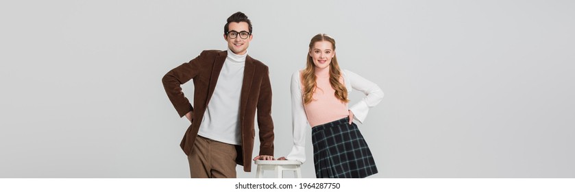 joyful couple in retro clothes posing with hands on hips near high stool isolated on grey, banner - Shutterstock ID 1964287750