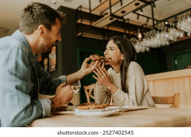 A joyful couple shares a moment at a rustic restaurant, savoring slices of pizza while laughing together and enjoying the vibrant atmosphere around them. - Powered by Shutterstock