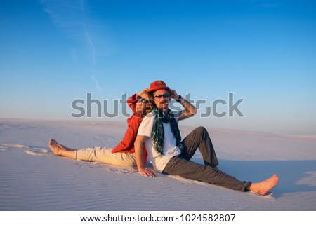 Joyful couple sitting, back to back, in the desert against a blue sky on a sunny evening, laughing and having fun. Happy people get new impressions and enjoy life during travel and tourism.