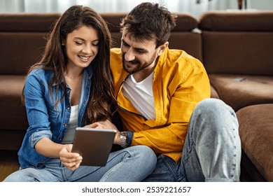 A joyful couple sitting on the living room floor, engaging with a tablet. They appear relaxed and happy, showcasing a moment of togetherness and connection at home. - Powered by Shutterstock