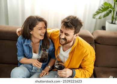 A joyful couple sitting on a sofa, enjoying glasses of wine and sharing laughter. The image conveys happiness, relaxation, and a sense of togetherness in a comfortable home setting. - Powered by Shutterstock