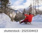 Joyful couple slides on a snow sled through a beautiful snowy forest