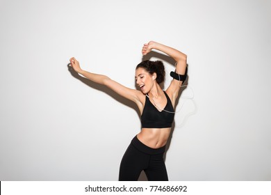 Joyful Curly Brunette Fitness Woman Listening Music By Smartphone And Dancing Over White Background