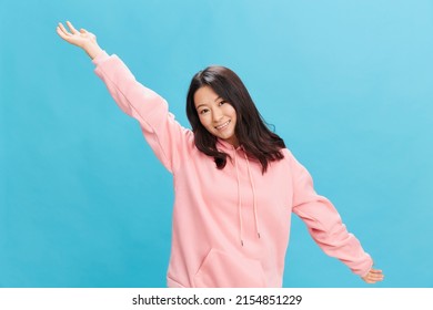 Joyful cute Asian student young lady in pink hoodie sweatshirt spreads hands posing isolated on over blue studio background. The best offer for ad. People Emotions for Everyday concept - Powered by Shutterstock