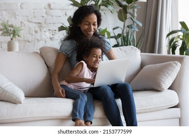 Joyful Cute Preschool Girl And Happy Black Mom Using Laptop Together, Watching Funny Cartoon Movie, Laughing, Speaking On Video Call, Shopping Online Together. Family Communication Concept