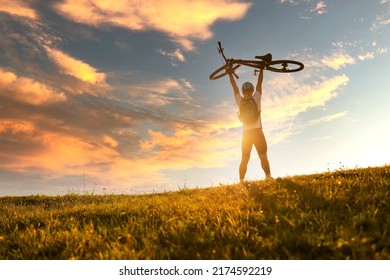 Joyful cyclist celebrating victory holding his bicycle over himself on the dramatic sky sunset background. Concept of a sports people success victory. Mountain biker. Active healthy happy lifestyle.