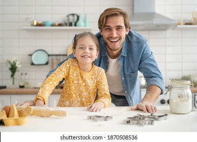 Fröhlicher Vater und Tochter, die sich beim Kneten des Teiges auf dem Küchentisch amüsieren und zusammen backen