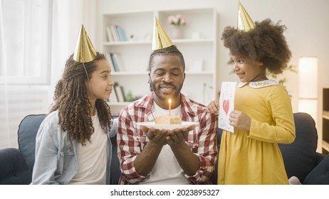 Joyful Dad In Party Hat Blowing Out Birthday Cake Candle, Celebrating With Daughters