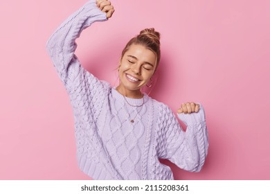 Joyful Dancing Woman Shakes Arms Has Eyes Closed Expresses Happiness And Upbeat Emmotions Wears Loose Knitted Sweater Isolated Over Pink Background Feels Carefree Dances With Rhythm Of Music