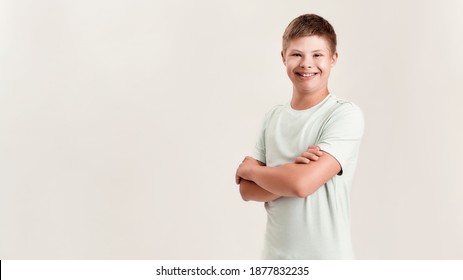 Joyful disabled boy with Down syndrome smiling at camera while posing, standing with arms crossed isolated over white background. Children with disabilities and special needs concept. Web Banner