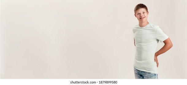 Joyful disabled boy with Down syndrome smiling at camera while posing, standing isolated over white background. Children with disabilities and special needs concept. Web Banner