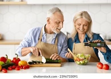 Joyful elderly couple enjoying cooking together in home kitchen, senior man chopping vegetables and woman adding dressing to salad, happy older spouses having fun while preparing healthy lunch - Powered by Shutterstock