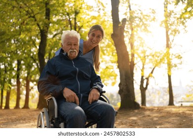 Joyful elderly man in a wheelchair going for a walk with a nurse, both smiling in a sunlit park with autumn trees - Powered by Shutterstock