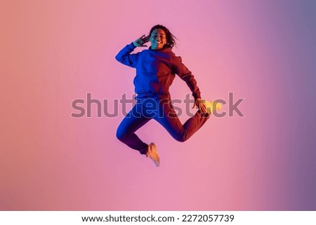 Joyful energetic black woman in sportswear having fun and jumping high on neon colorful studio background, full length, free space, banner