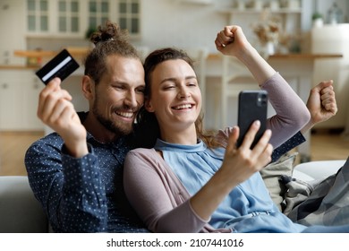 Joyful euphoric young family couple making yes gesture celebrating purchasing early birds tour or making profitable deal, paying for goods or services in mobile application using credit banking card.