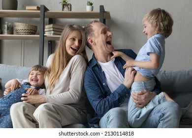 Joyful Excited Parents Tickling Funny Little Kids At Home. Pregnant Mom And Happy Dad Playing Active Games With Two Siblings Son And Daughter, Laughing, Screaming, Enjoying Family Leisure Time