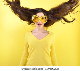 Joyful Excited Surprised Young Woman With Flying Hair And Big Funny Glasses Over Yellow Background. 
