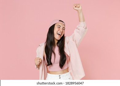 Joyful excited young asian woman 20s in casual clothes cap clenching fists like winner isolated on pastel pink wall background studio portrait. People emotions lifestyle concept. Mock up copy space.