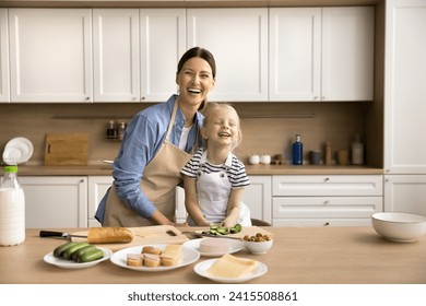 Joyful excited young mom and pretty little daughter girl preparing sandwiches in kitchen together, cutting ingredients, looking at camera, smiling, laughing, posing for cooking blog picture - Powered by Shutterstock