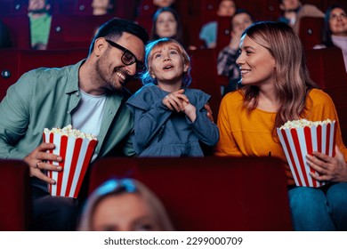 A joyful family is bonding in cinema, enjoying the movie with their child, eating popcorn and having fun. - Shutterstock ID 2299000709