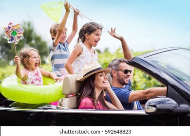 A joyful family, in a convertible car, goes on holiday to the sea. Children have colorful buoys and landing nets. Focus on the mother - Shutterstock ID 592648823