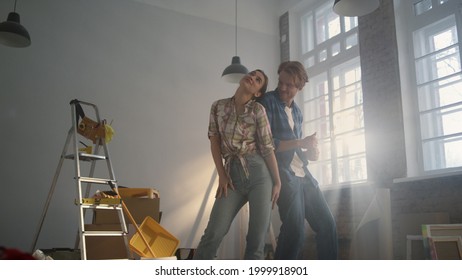 Joyful Family Dancing Together In New Home With Construction Tools. Happy Woman And Man Having Fun Indoors. Cheerful Couple Enjoying House Renovation Inside.