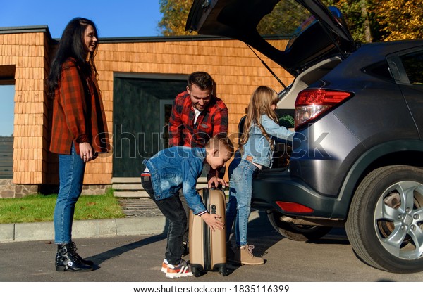 Joyful\
family helping each other to unload auto\'s trunk from carton boxes\
and suitcases during moving to new\
apartment