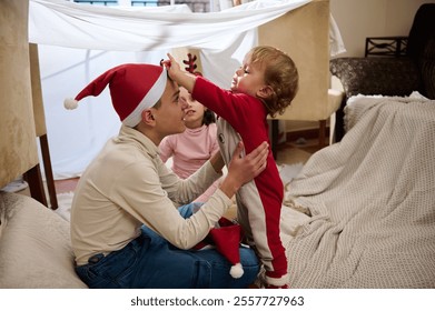 Joyful family moments captured as children build a festive blanket fort with parents. Perfect for depicting holiday fun and family bonding during the Christmas season. - Powered by Shutterstock