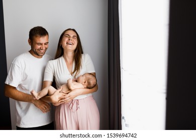 Joyful Family Moments. Young Extremely Happy Mother And Father Holding Their Newborn Baby And Laughing. Side Light, Room For Text.