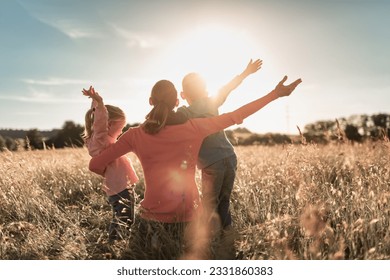 Joyful family morning in the countryside, mother and children raise arms in a field with feelings of happiness and togetherness.