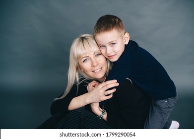 Joyful Family Mother And Her Son In Black Clothes Are Posing In Studio With Dark Background. Family Portrait