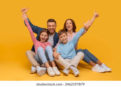 A joyful family sits closely together with arms raised in a celebratory gesture, smiling enthusiastically. A father and mother are behind their daughter and son, all sharing a moment of happiness - Powered by Shutterstock