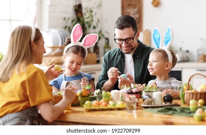 Joyful family wearing bunny ears headbands gathering at table in modern light kitchen   paining Easter eggs together