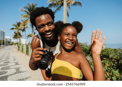 A joyful father and daughter enjoy a sunny day at the beach. The daughter waves happily while the father holds a camera, capturing memories. A perfect, carefree and happy family moment in nature. - Powered by Shutterstock