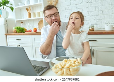 Joyful father and daughter sit at the  laptop in cozy sunny kitchen at home eating corn sticks. Kitchen design, furniture for kitchen. Amicable, happy family. - Shutterstock ID 2147989881